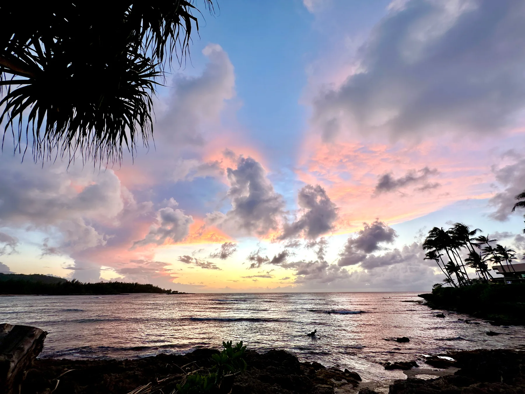 Una costa tropical al atardecer, con nubes coloridas reflejadas en el agua.