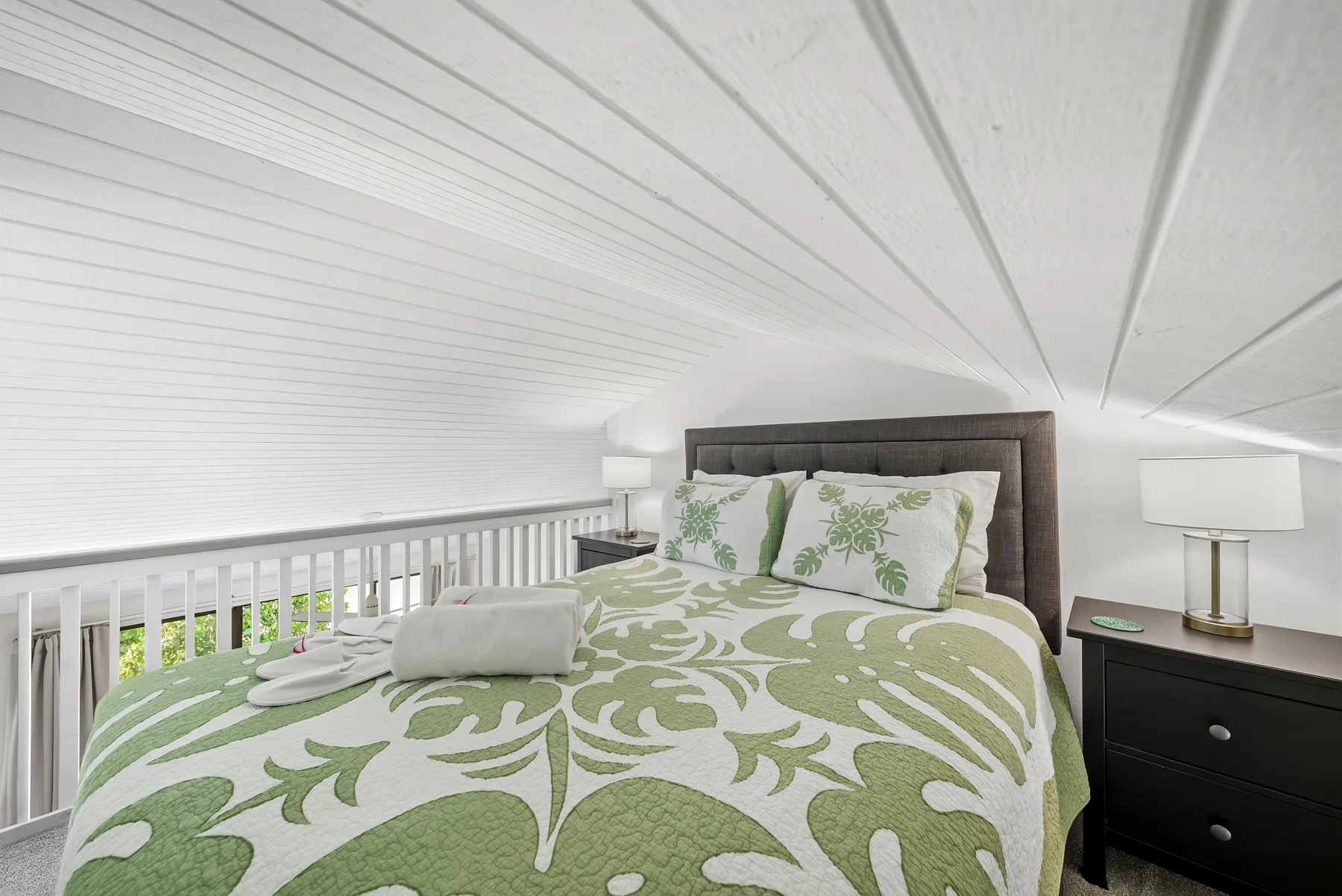 Un dormitorio con una cama cubierta con ropa de cama estampada en verde y blanco bajo un techo inclinado.