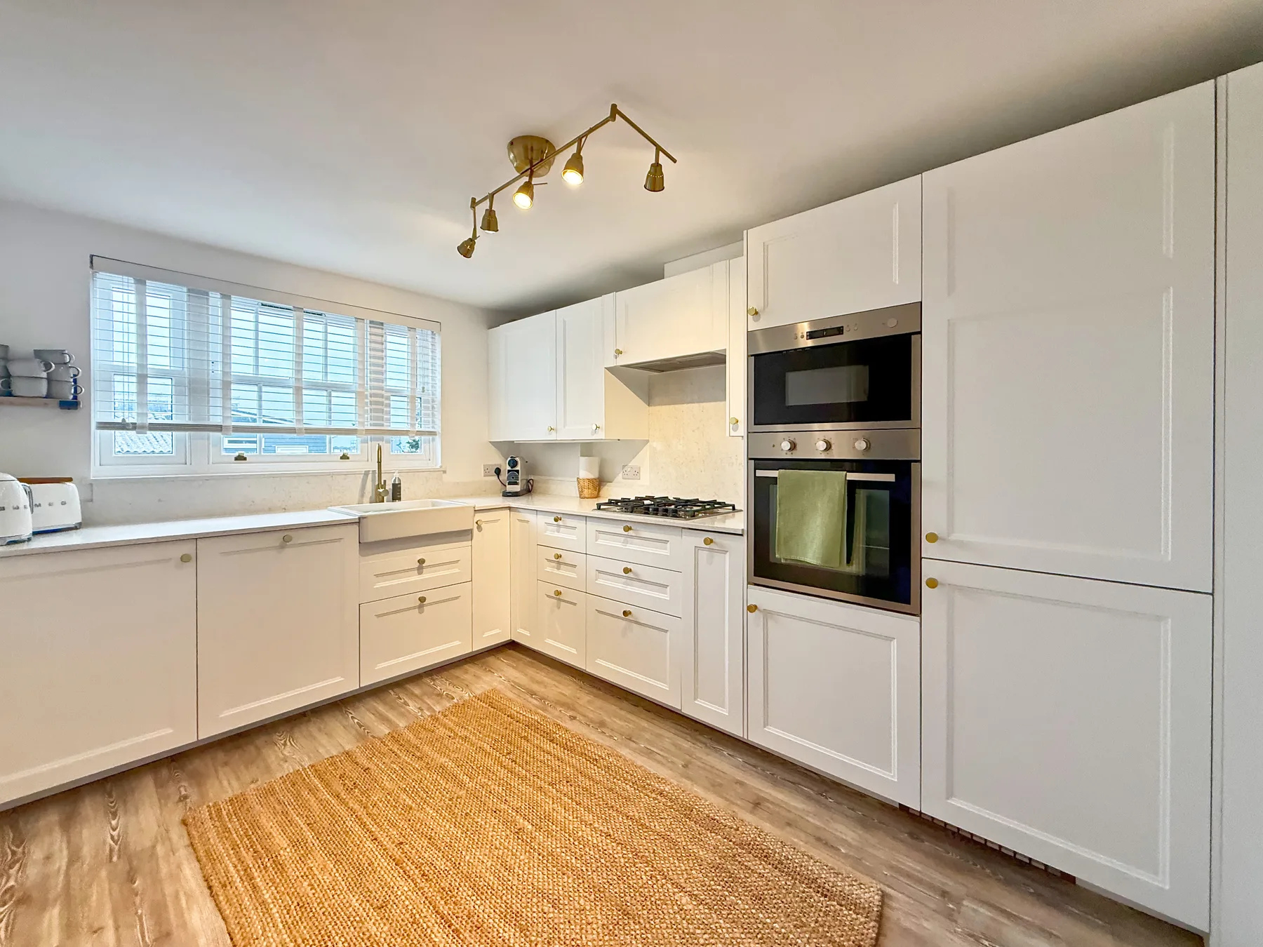 Una cocina luminosa con gabinetes blancos, una encimera y una alfombra tejida.
