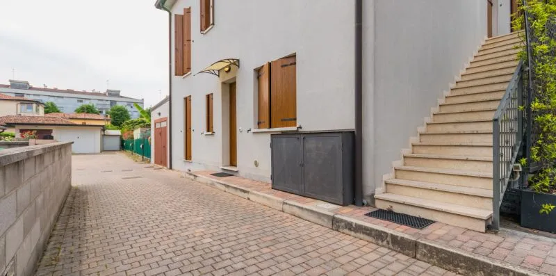 A paved courtyard runs alongside a white building with an exterior staircase.