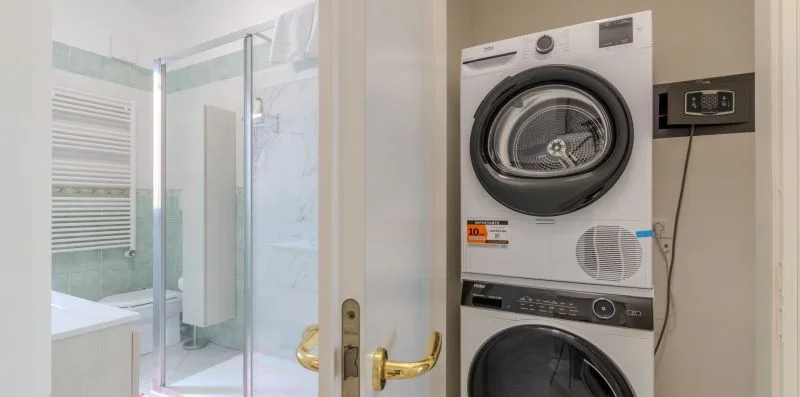 A bathroom with a glass shower and a stacked washer and dryer.