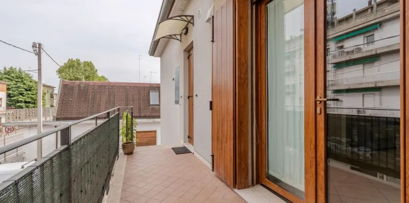 Un pasillo de balcón embaldosado junto a puertas de vidrio y una barandilla metálica.