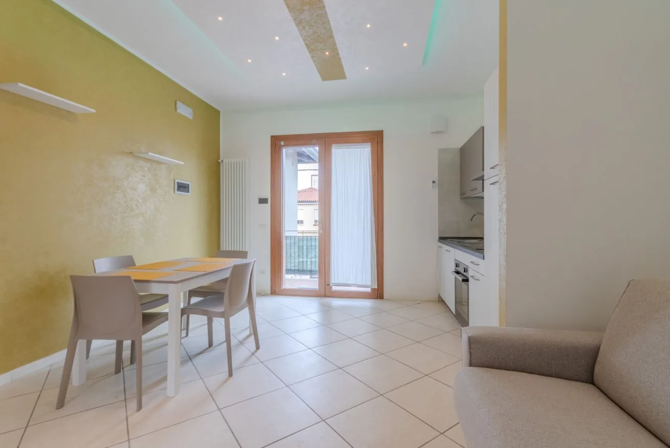 A dining area beside a compact kitchen, with doors opening onto a balcony.