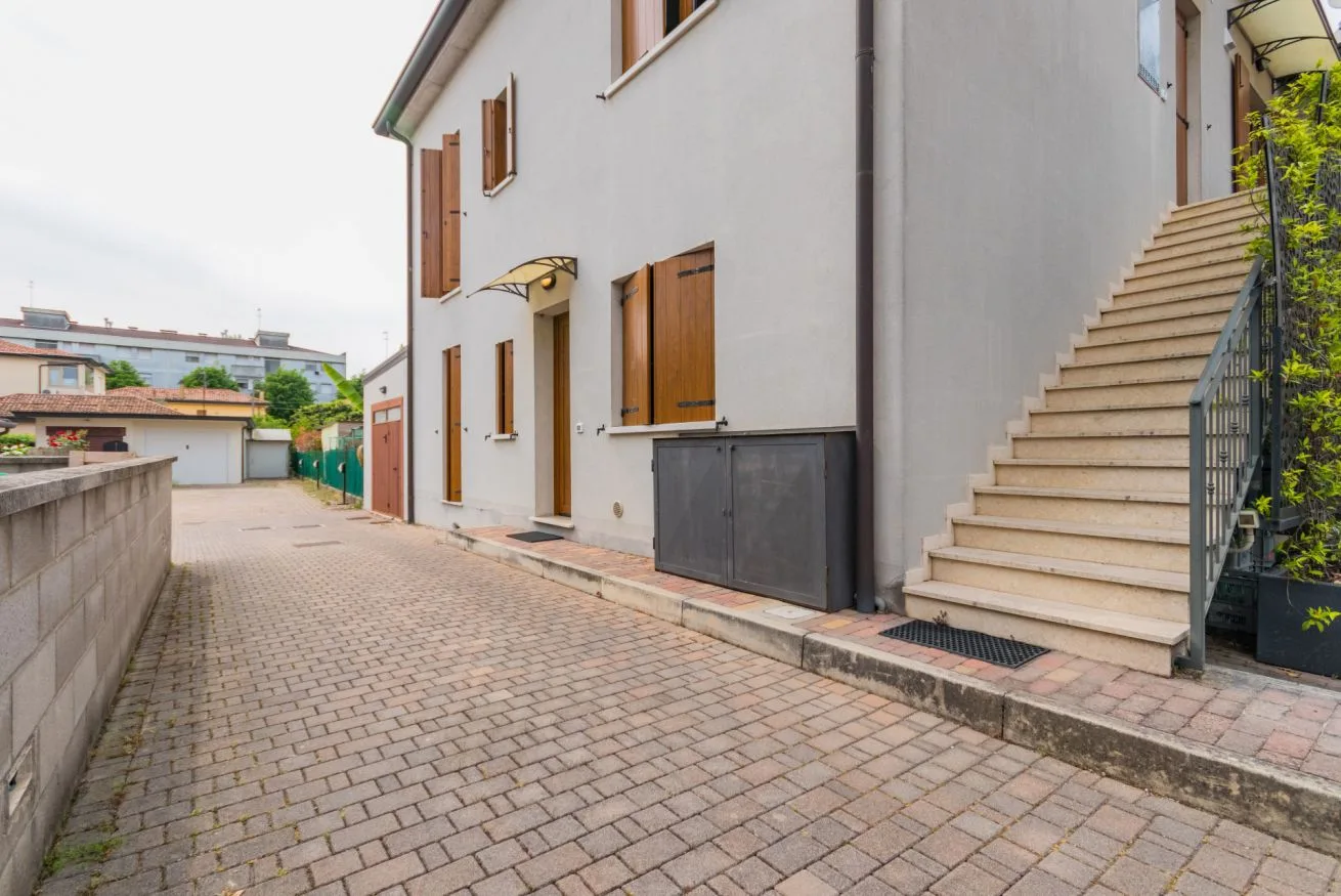 A paved walkway runs beside a building with an outdoor staircase.