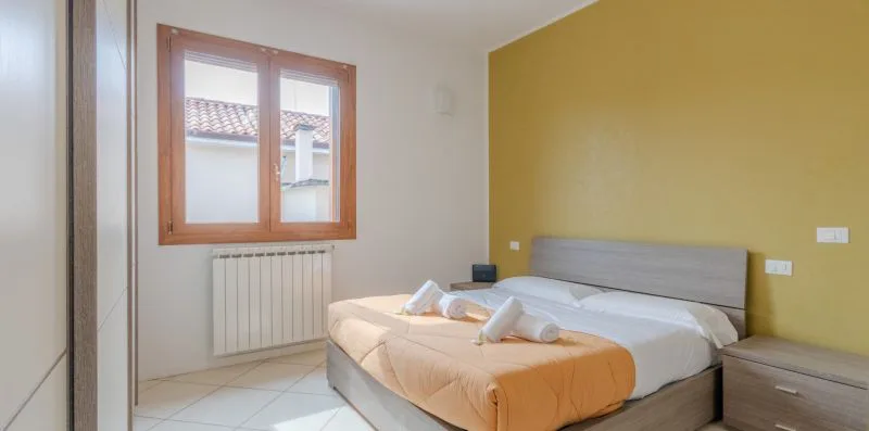 Un dormitorio con una cama, cajones junto a la cama y una ventana sobre un radiador.