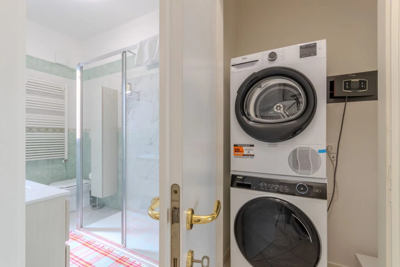 A bathroom with a glass shower beside a stacked washer and dryer.