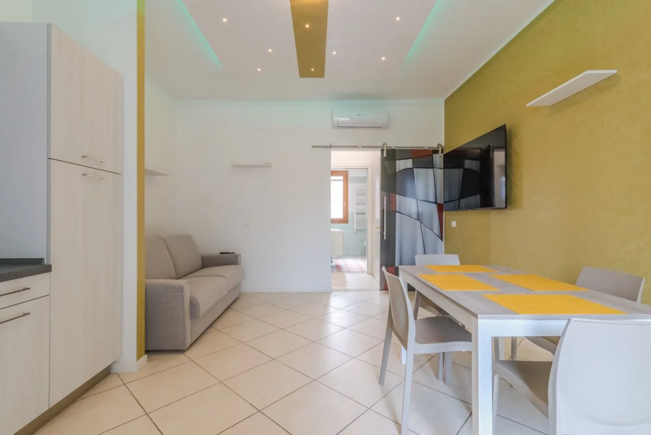 A bright living and dining area with a sofa, table, and wall-mounted television.