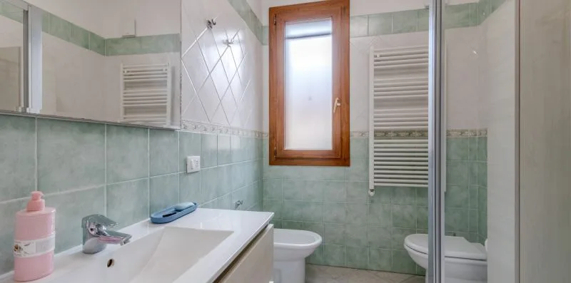 A tiled bathroom with a sink, toilet, and window.