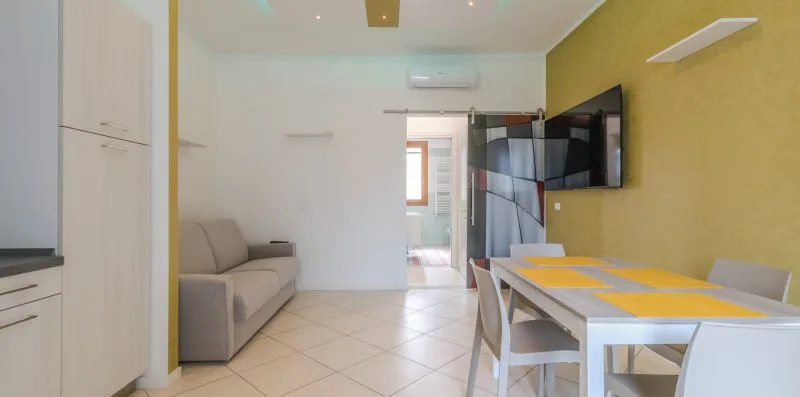 Una luminosa sala de estar y comedor con sofá, mesa y televisor en la pared.
