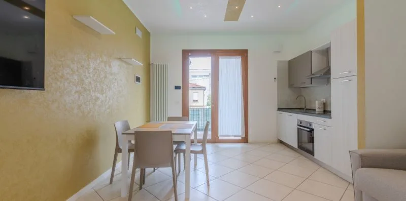 A bright dining area with a table and kitchenette beside glass doors.