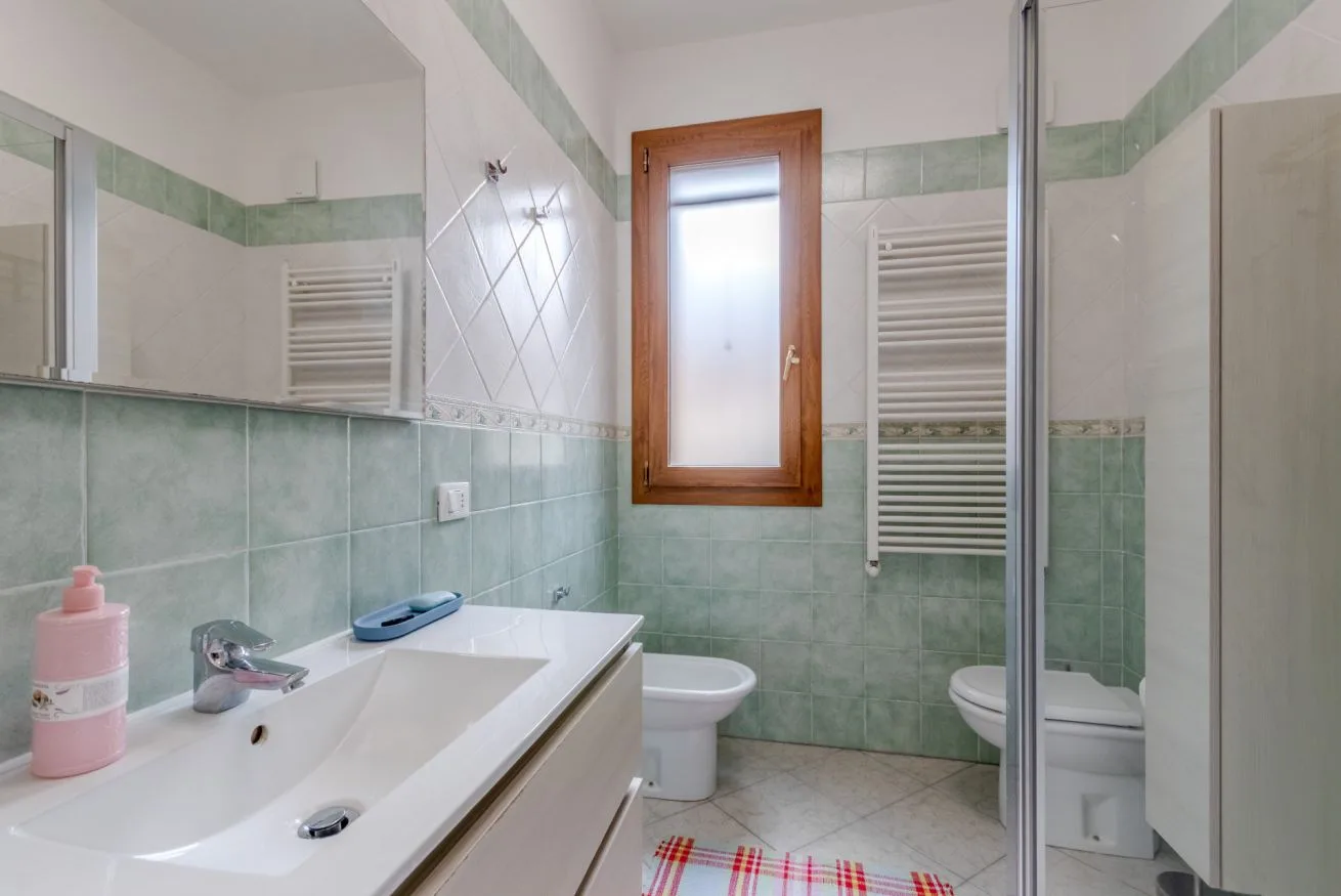 A tiled bathroom with a sink, toilet, and frosted window.