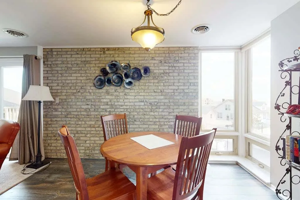 A dining area with a wooden table and chairs beside large windows.
