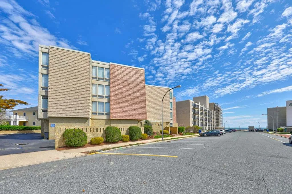 A large paved parking area sits in front of a multi-story building under a blue sky.