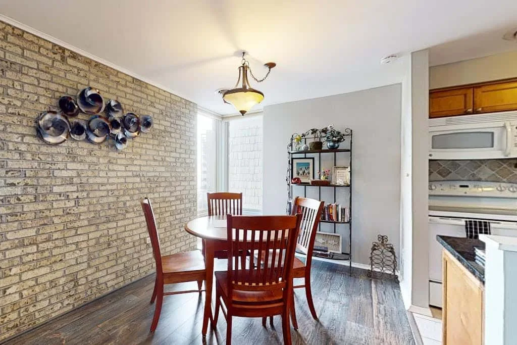 A dining area with a wooden table and chairs beside a brick wall.