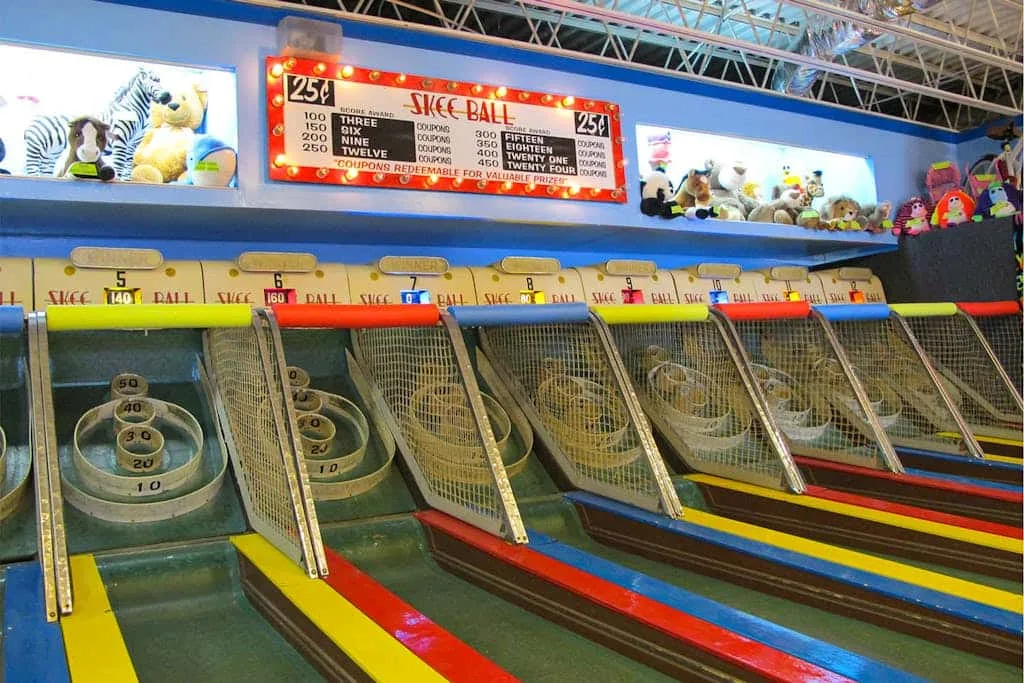 A skee-ball arcade game with colorful lanes and plush prizes displayed above.