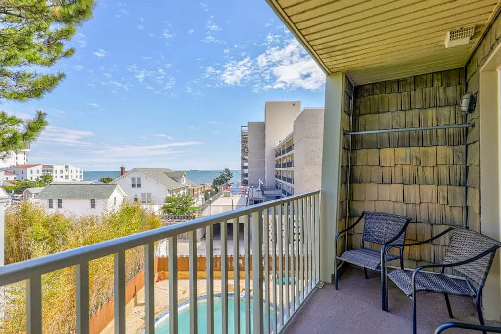 A balcony with outdoor seating overlooks nearby buildings and the water.