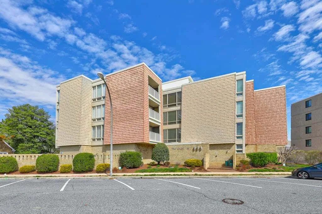 A multi-story brick building stands beside a paved parking area.