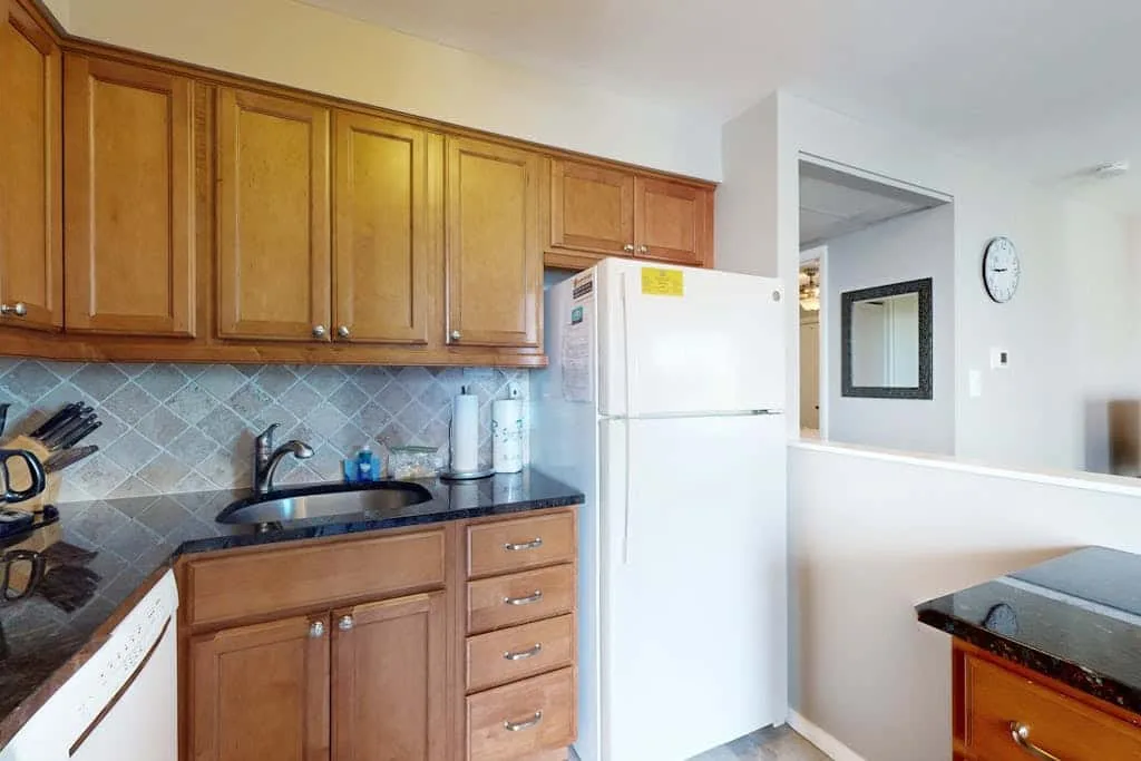 A kitchen with wooden cabinets, a refrigerator, and a tiled backsplash.