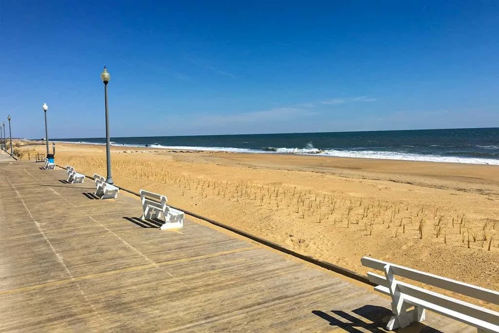 A seaside promenade with benches beside a sandy beach and ocean.