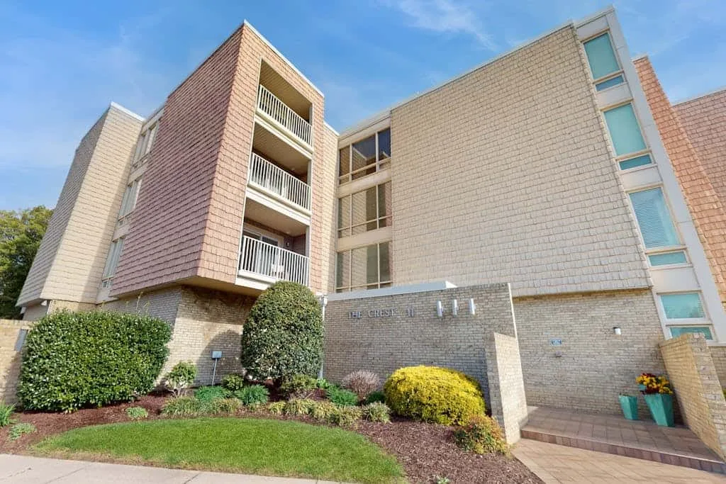 Exterior view of a multi-story brick building with landscaped shrubs and a walkway.