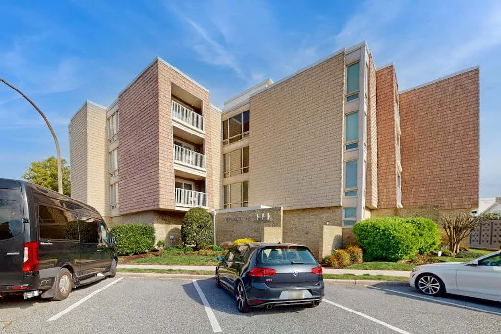 A multi-story brick building stands beside a parking area with parked vehicles.