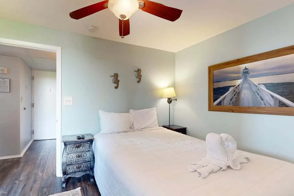 A bedroom with a neatly made bed and framed coastal artwork.