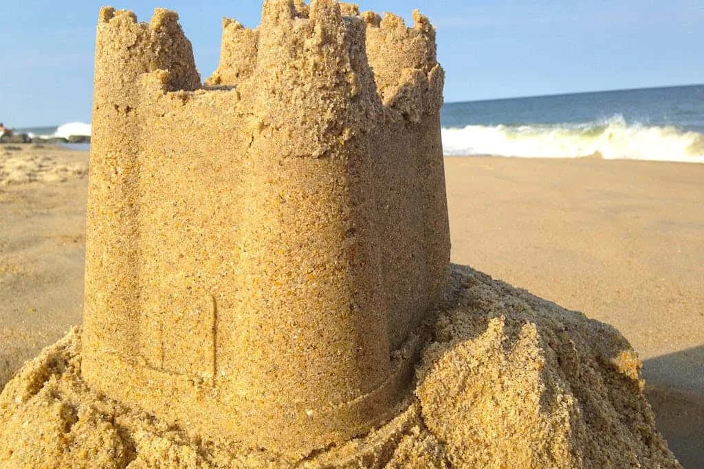 A large sandcastle stands on a beach beside the ocean.