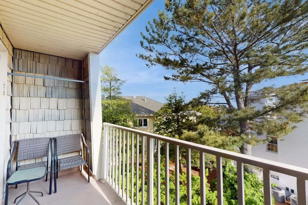 A covered balcony overlooks nearby homes and leafy trees.