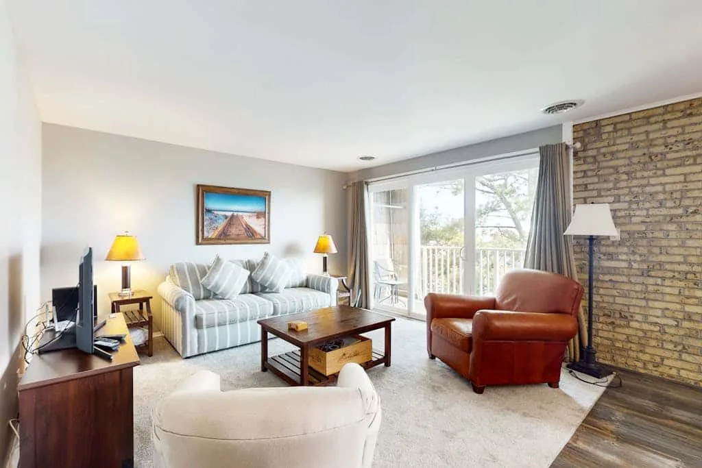 A living room with seating around a coffee table beside large windows.
