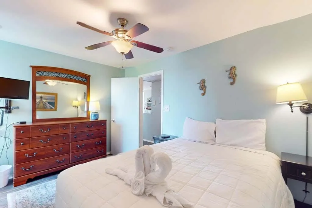 A bedroom with a neatly made bed, dresser, and ceiling fan.
