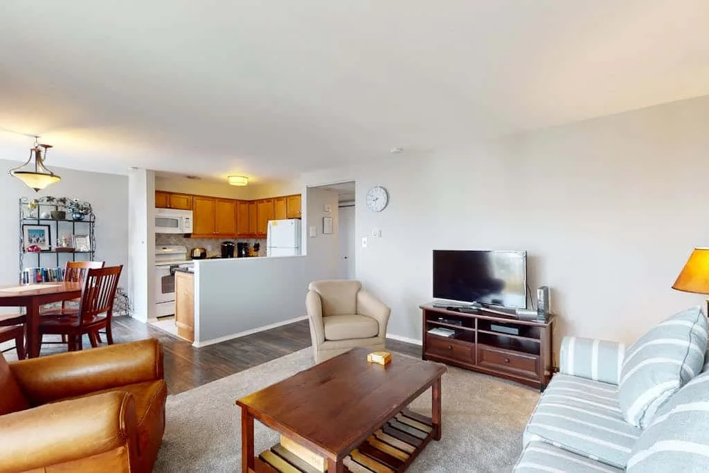 An open-plan living and dining area with a kitchen beyond, furnished with seating and a coffee table.