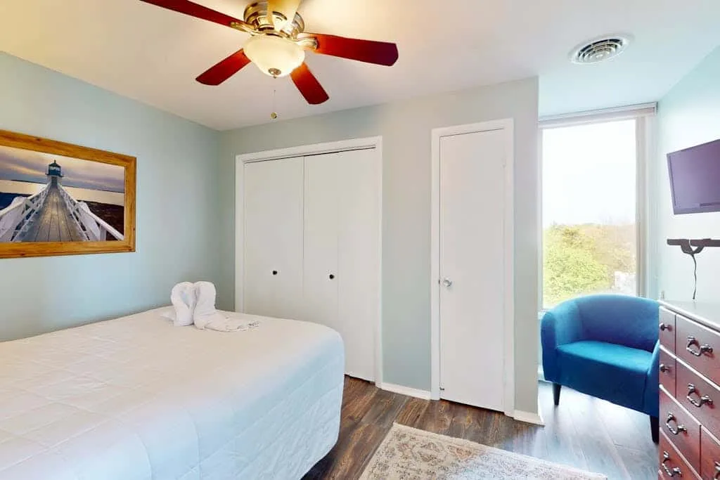 A bedroom with a bed, a blue armchair, and a window.