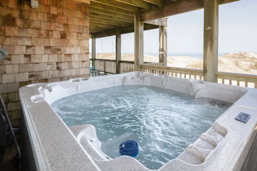 A bubbling hot tub sits on a covered deck overlooking the ocean.