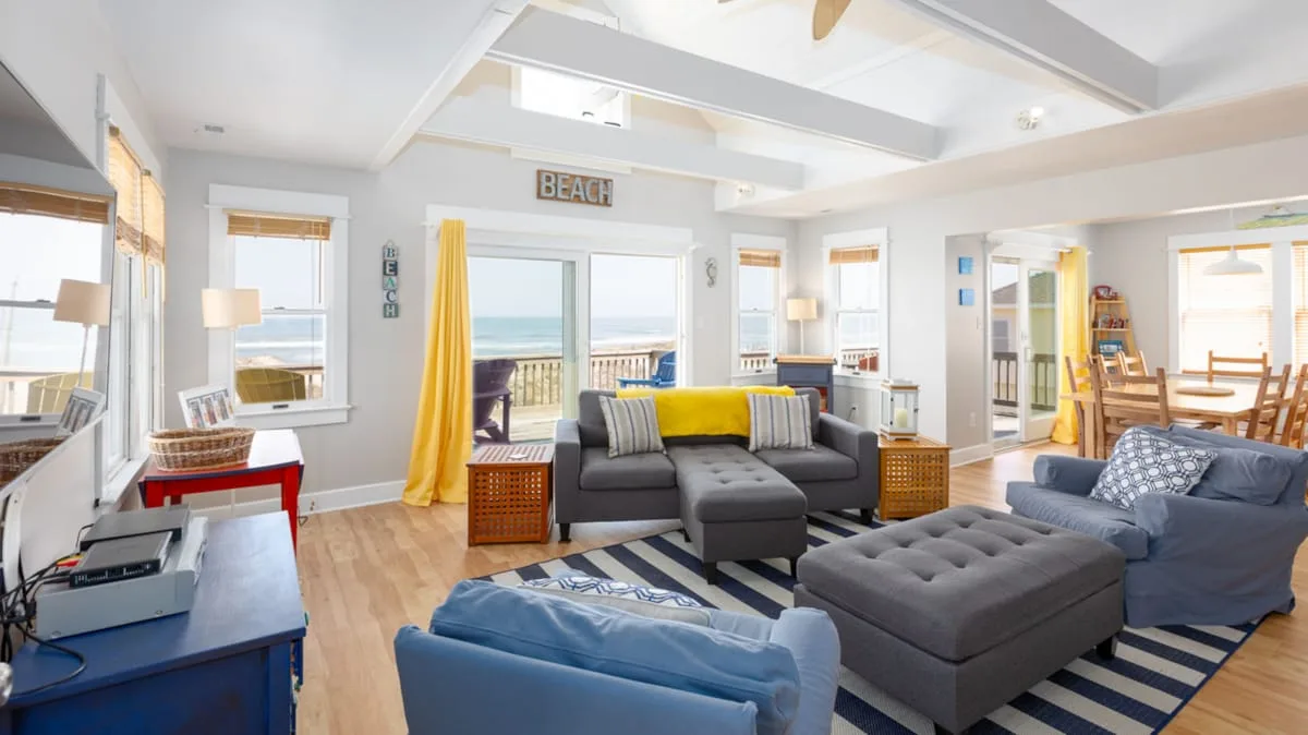 A bright living room with sofas, an ottoman, and a dining area.