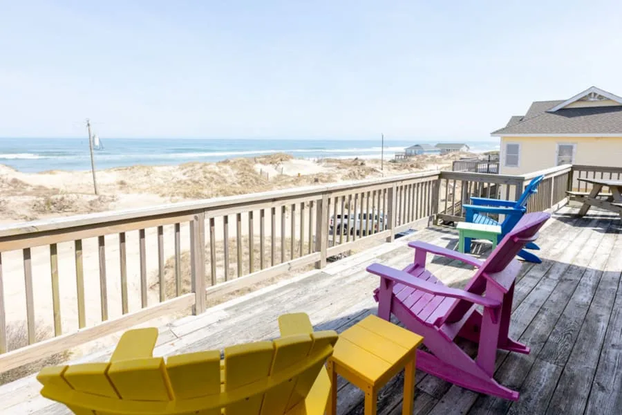 A seaside deck with colorful seating overlooks sandy dunes and the ocean.