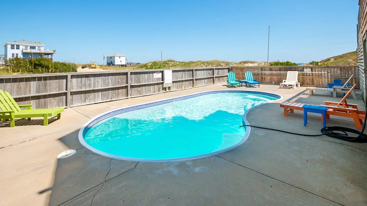 An outdoor swimming pool sits on a paved deck with seating around it.