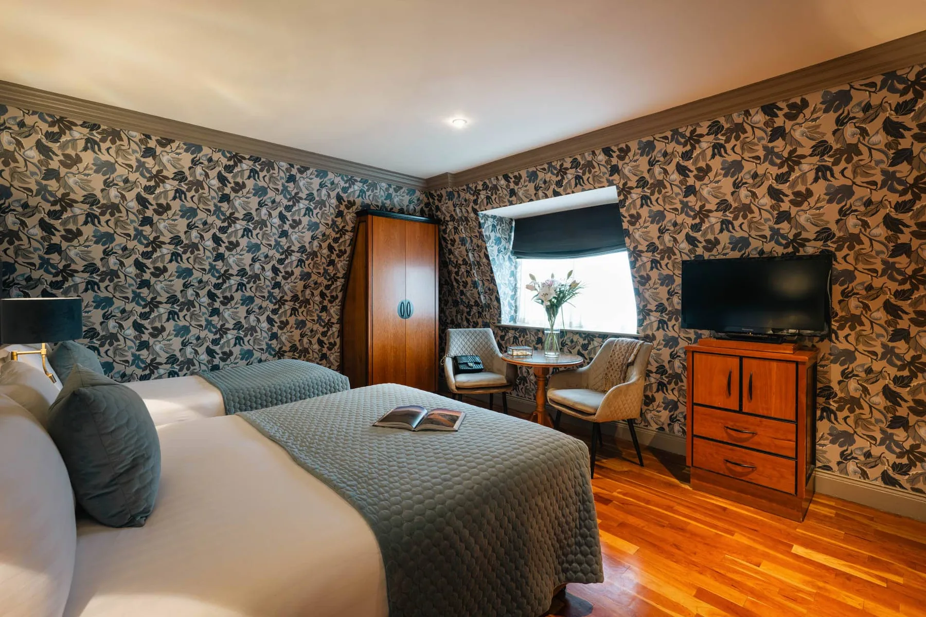 Habitación superior con dos camas, suelo de madera, zona de estar junto a la ventana y televisión.