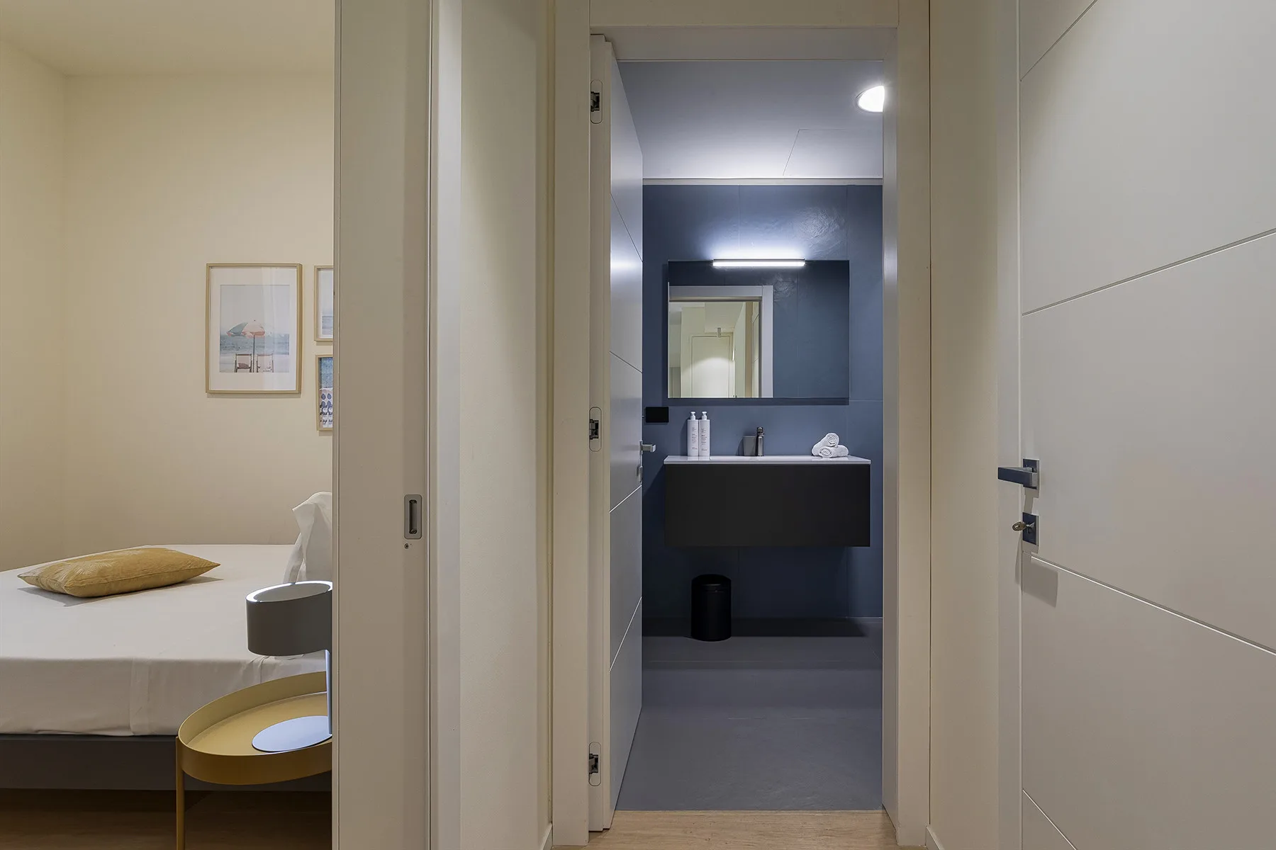 A bedroom opens onto a bathroom with a dark vanity and mirror.