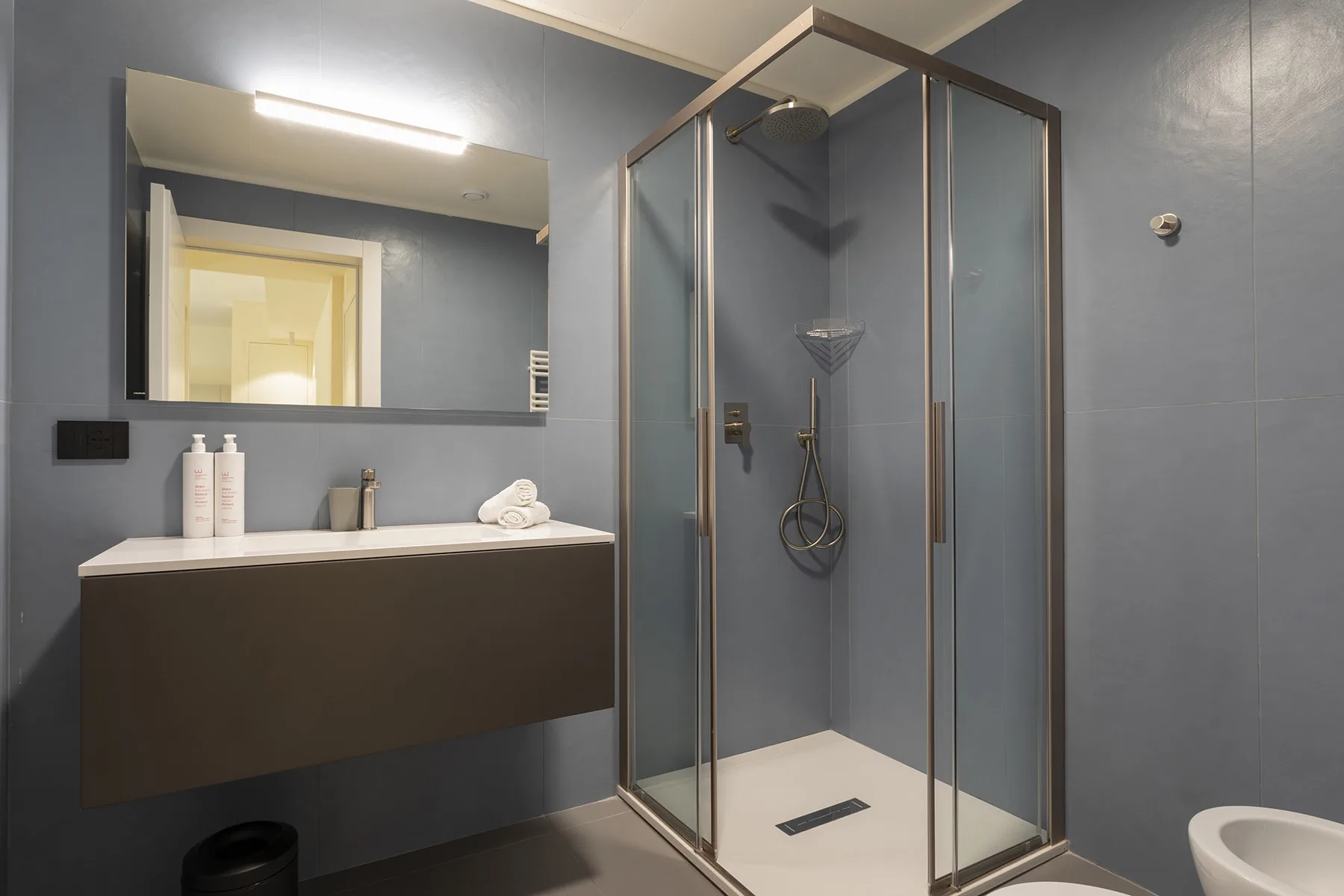 A modern bathroom with a glass shower and a sink beneath a wide mirror.