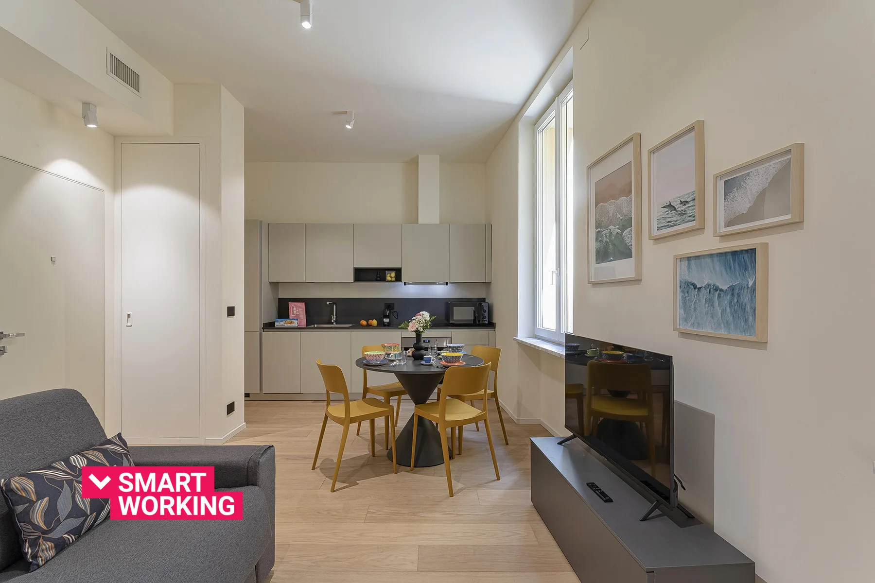 A bright living and dining area with an open kitchen and wall-mounted television.