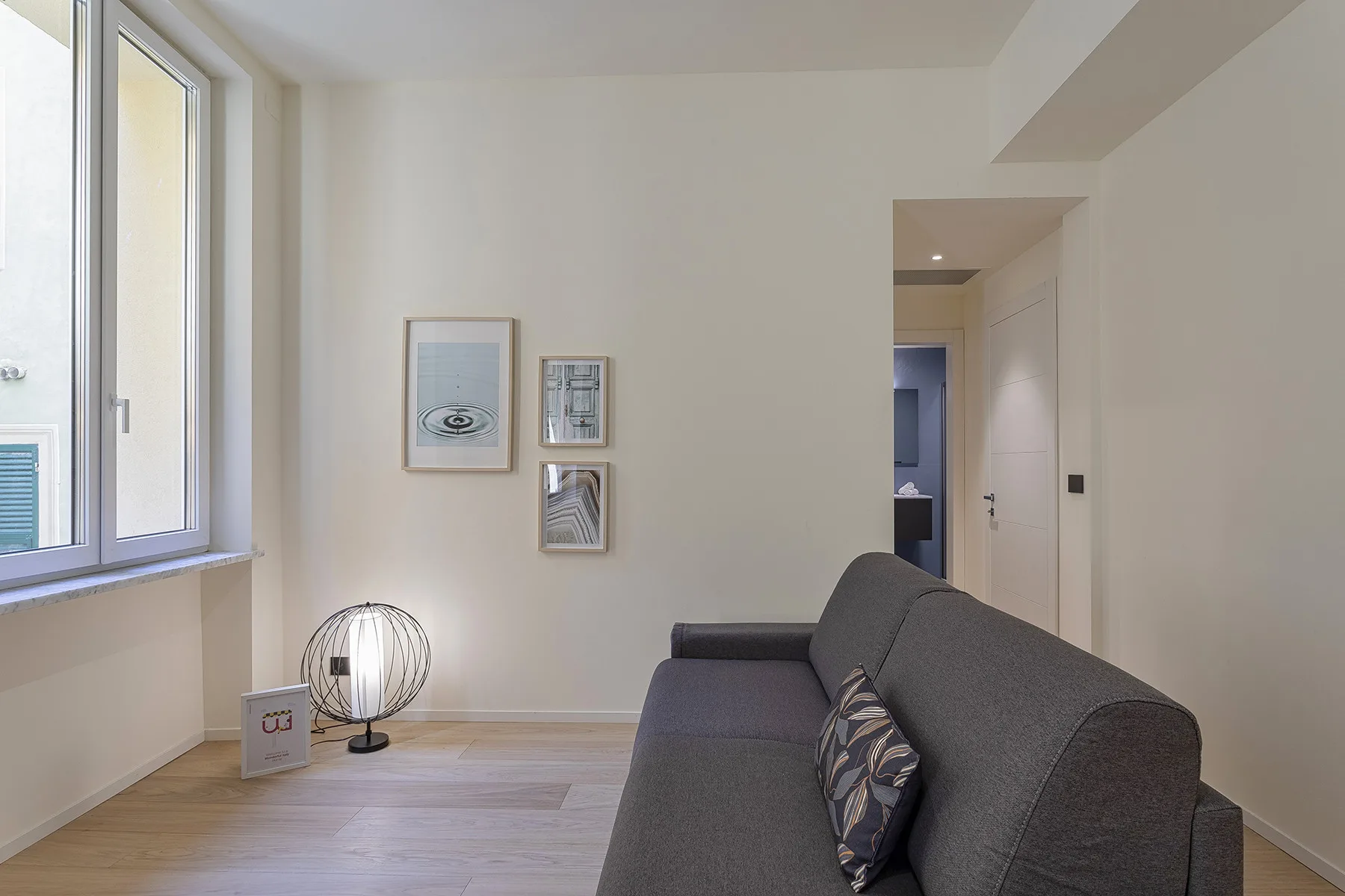 A bright living room with gray seating, framed prints, and a large window.