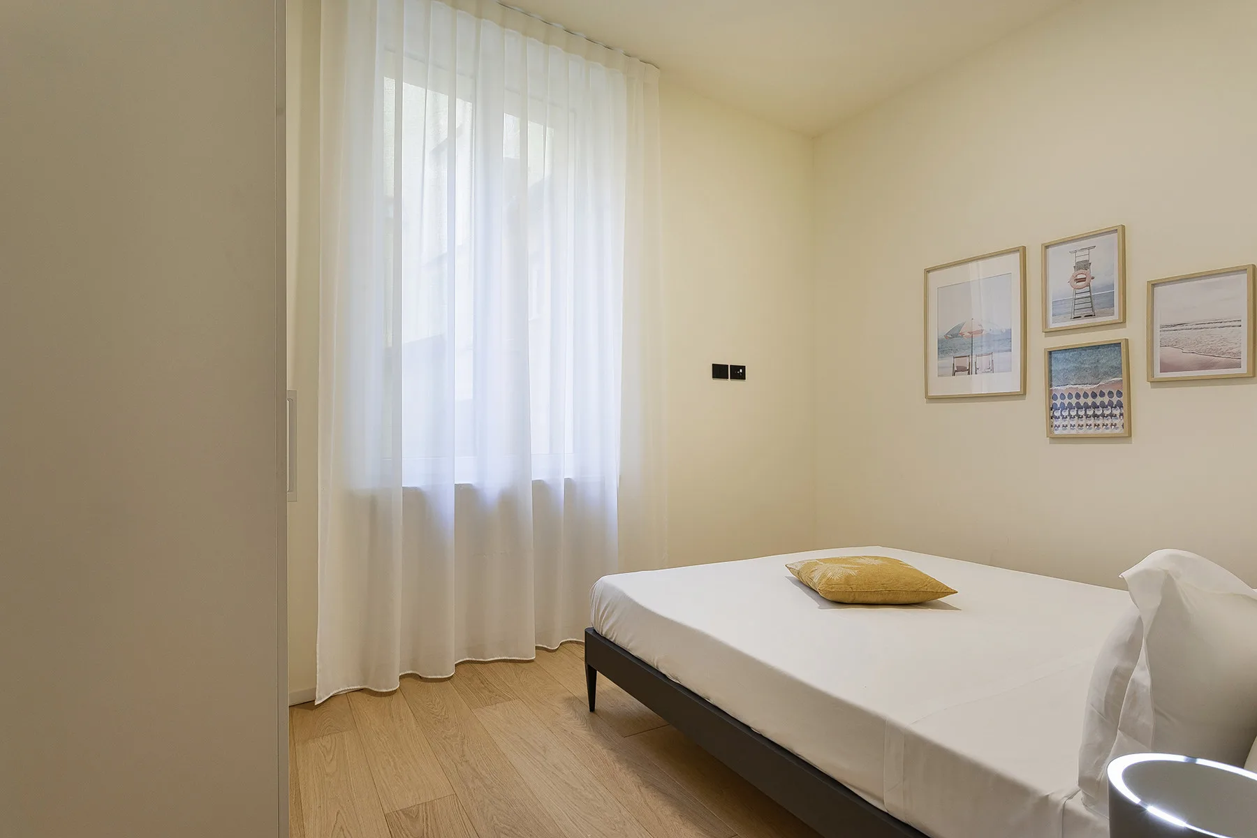 A bedroom with a bed, sheer curtains, and framed pictures on the wall.