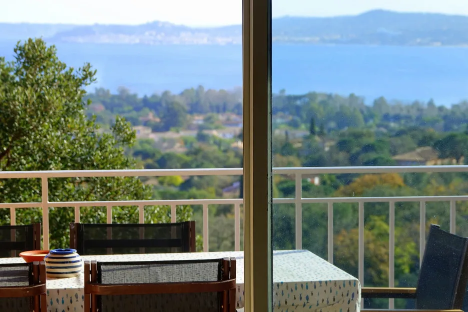 A balcony dining area overlooks green hills and a body of water.