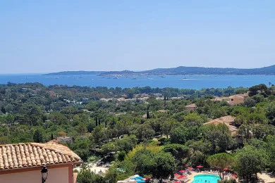 A coastal landscape overlooks a wooded area, rooftops, and a swimming pool.