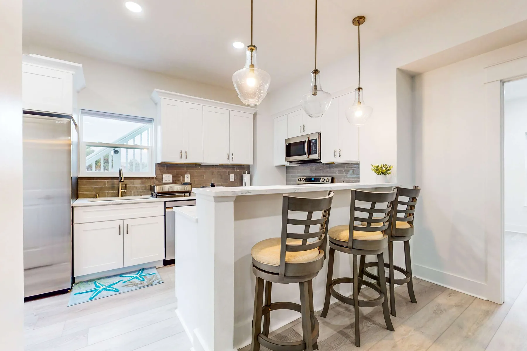 A bright kitchen with a counter, bar seating, and white cabinetry.