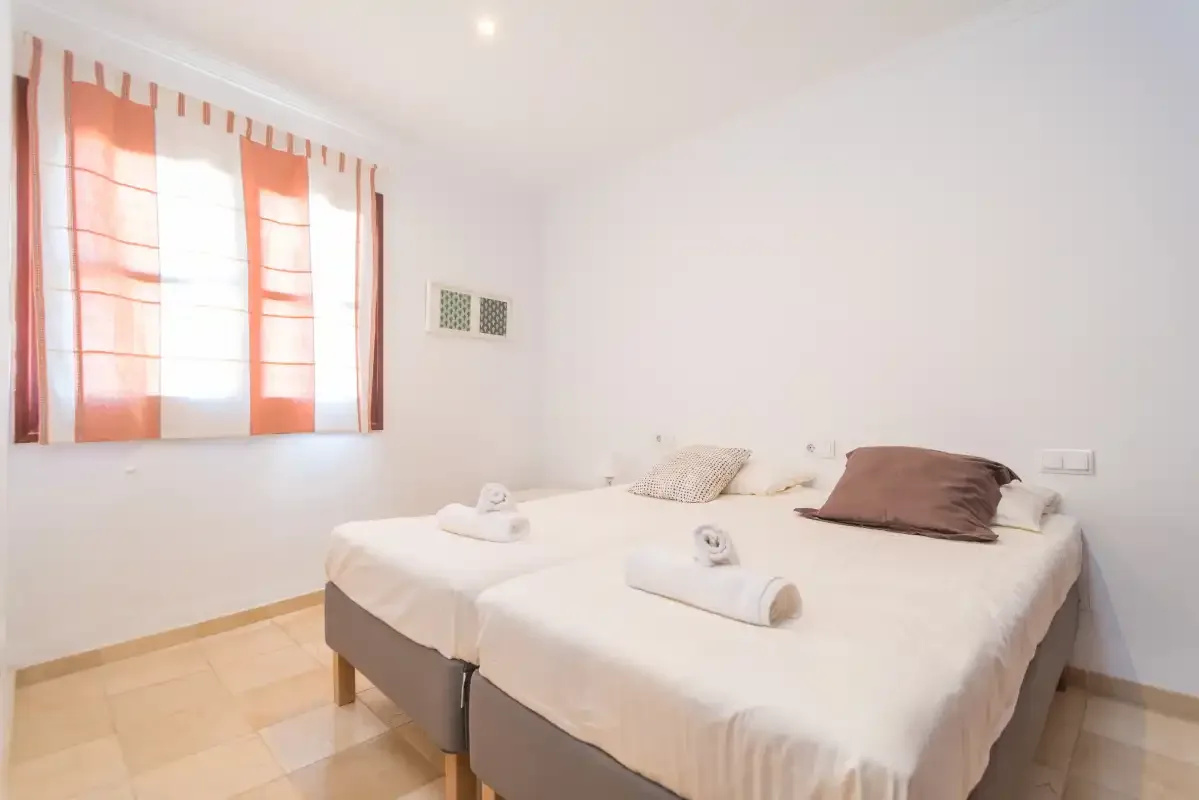 A bedroom with two beds beneath a window with orange curtains.