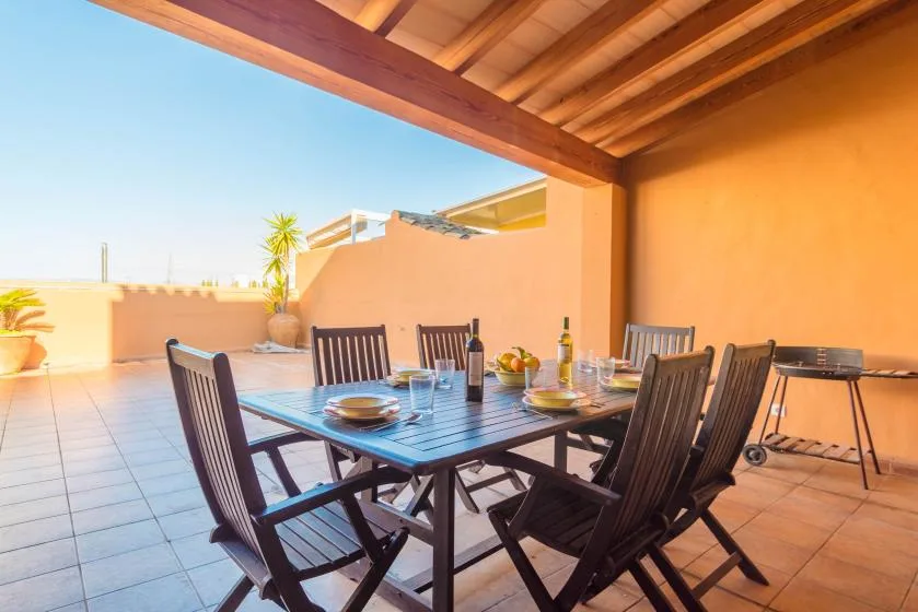 Comedor exterior cubierto con una mesa de madera y sillas.