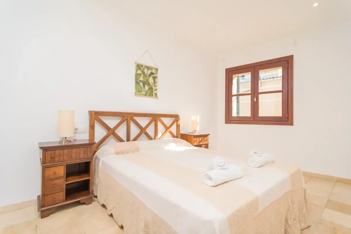 A bright bedroom with a double bed, wooden bedside tables, and a window.