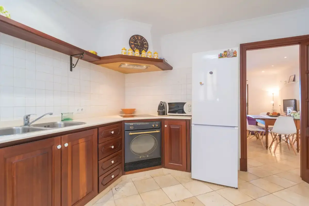 A bright kitchen with wooden cabinets, a washing machine, and a refrigerator.