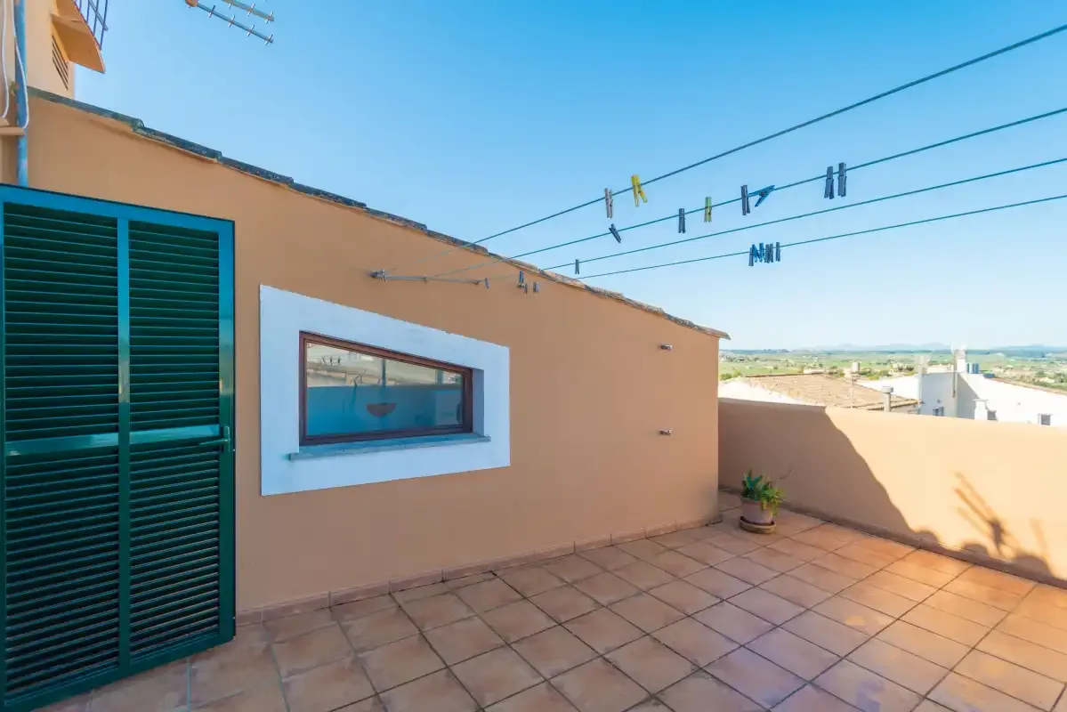 A tiled rooftop terrace beside a peach-colored wall with a small window.